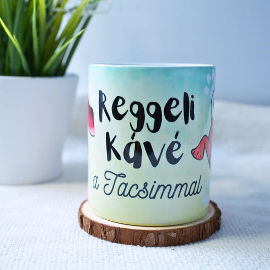 Reggeli kávés bögre fa alátéten, kézzel készült egyedi Zsempiri dizájnnal, növény háttérben.